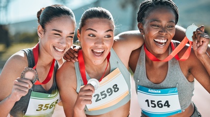 Drei Personen in Sportoutfits halten in den Händen jeweils eine Medaille und halten diese etwas nach oben