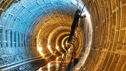 Eine Person steht auf einer Leiter in einem U-Bahn-Tunnel und schweißt etwas an der Tunnelwand.