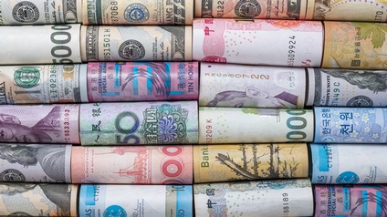 Nahaufnahme mehrerer, nebeneinander liegender, eingerollter Geldscheine in verschiedenen Währungen, zum Beispiel Dollar