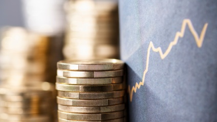 Vier Stapel Münzen sind neben einem grauen Display, auf dem ein Aktienkurs abgebildet ist