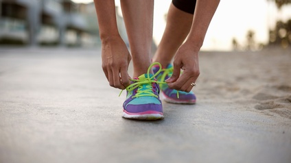 Detailansicht auf bunten Sportschuh einer Person, die sich gerade die Schnürsenkel zu Masche bindet, ringsum verschwommen Sand und Strandumgebung