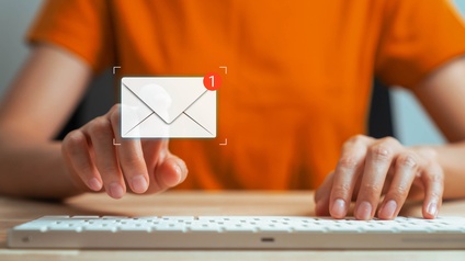 Frontale Aufnahme der Hände einer Person, die auf einer Computertastatur tippt. Über der Tastatur ist ein Icon eines Briefumschlags. An der rechten oberen Ecke des Briefumschlags ist eine weiße eins in einem roten Kreis