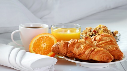 Frühstück mit Kaffee, einem Glas Orangensaft Müsli und Croissants auf einem Tablett in einem Bett platziert