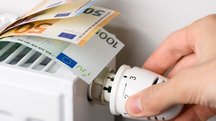 Verschiedene Euroscheine liegen auf einer Heizung mit Heizkörperthermostat