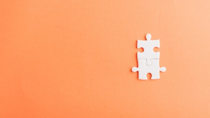 Zwei ineinander passende, weiße Puzzleteile vor orangem Hintergrund in der rechten Bildhälfte