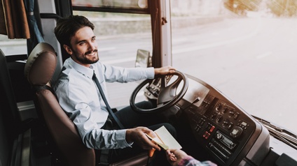 Lächelnde Person an Lenkrad eines Autobusses sitzend nimmt Papier anderer Person entgegen