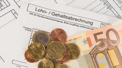 Verschiedene Euromünzen und Euroschein liegen auf einer Lohn- und Gehaltsabrechnung
