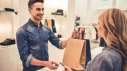 Verkäufer überreicht einer Kundin die Einkaufstaschen