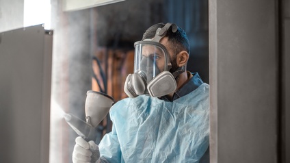 Porträt einer Person mit Vollgesichtsmaske in Overall besprüht mit Farbsprühsystem Oberfläche