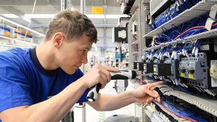 Person mit Schraubmaschine repariert Board mit elektrotechnischen Apparaturen
