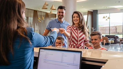 Ein Paar mit zwei Kindern an der Hotelrezeption beim Einchecken