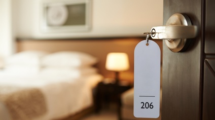Detailansicht Türklinke mit Schlüssel samt Anhänger mit Aufschrift 126, im Hintergrund verschwommen Hotelzimmer