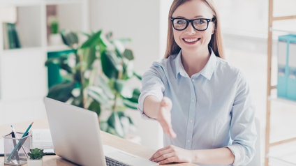 Person mit Brille sitzt an einem Schreibtisch und arbeitet mit einem Laptop