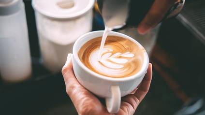 Nahaufnahme von einer Tasse Kaffee, die mit Milchschaum kreativ zu einem Muster gestaltet wird