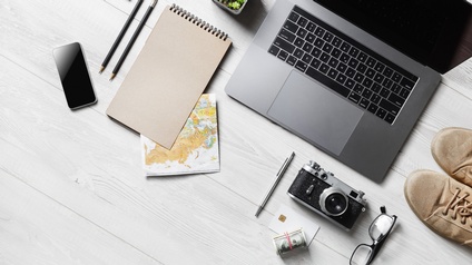 Laptop, Notizutensilien, Landkarte, Brille, Fotoapparat, Handy, Geld und Schuhe nebeneinander platziert