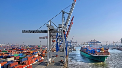 Beladenes Frachtschiff steht bei einem großen Container Terminal mit bunten Containern sowie Kränen