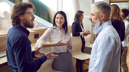 Personen in Businesskleidung stehen gemeinsam in einem modernen Büroraum und unterhalten sich