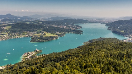 Aufnahme eines Teils des Wörthersees aus der Vogelperspektive. Das Wasser ist türkis. Am Ufer sind Häuser sowie grüne Wiesen und Bäume