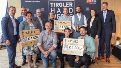 Mehrere Personen posieren vor einer großen „Tiroler Handwerkspreis“-Fotowand. Einige halten Urkunden, Trophäen und überdimensionale Schecks für den ersten, zweiten und dritten Platz in der Kategorie „Nachhaltigkeit & Regionalität“. Im Hintergrund sind die Logos des Tiroler Handwerkspreises und der Wirtschaftskammer Tirol sichtbar.