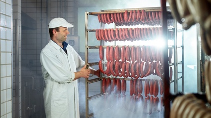 Lächelnde Person blickt auf Wurstwaren, die auf einem Metallwagen in einem Fleischereibetrieb stehen