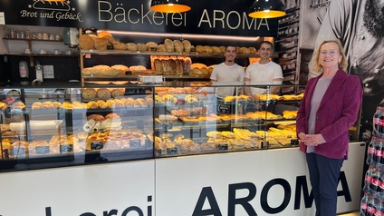 Nahaufnahme einer Person vor dem Tresen der Bäckerei Amora. Hinter dem Tresen ist eine weitere Person, die Teigwaren verkauft