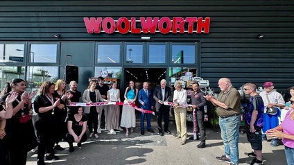 Eine Gruppe von Menschen steht vor der Filiale eines Geschäftes mit dem Schriftzug Woolworth. Einige halten ein Band mit der Aufschrift Woolworth