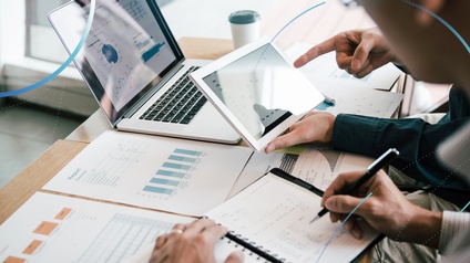 Zwei Personen sitzen vor einem Laptop an einem Tisch und arbeiten gemeinsam an Auswertungen und Diagrammen