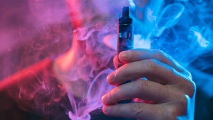 Mann raucht E-Zigarette und verschwindet in lilafarbenem und blauem Rauch