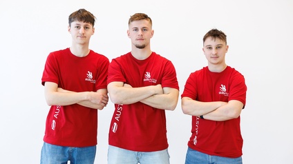 Drei junge Männer in roten T-Shirts mit verschränkten Armen vor weißem Hintergrund