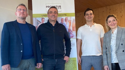 Vier Personen stehen nebeneinander in einem Innenraum vor einem Roll-up-Banner mit der Aufschrift „PRONATUR HAUS – Unsere Geschichte“.