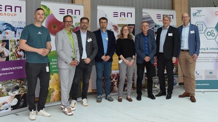 Gruppenfoto von mehreren Personen bei einer Fachveranstaltung, stehend vor Roll-up-Bannern der SAN Group und weiterer Organisationen in einem Innenraum.
