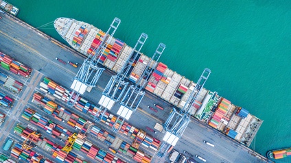 Luftaufnahme eines Containerfrachtschiffs, das zur Beladung in einem Hafen liegt.
