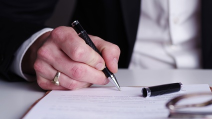 Eine Hand hält einen Stift und unterzeichnet ein Dokument
