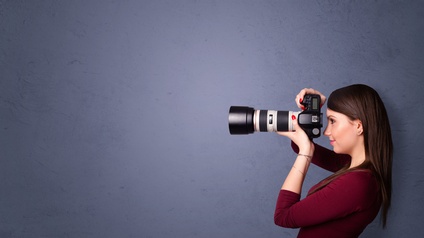 Person in Seitenansicht lugt durch Fotokamera, grauer Hintergrund