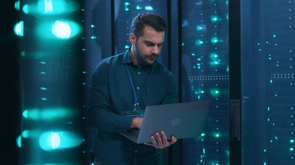 Person hält Laptop in der Hand und arbeitet im Stehen in einem Serverraum