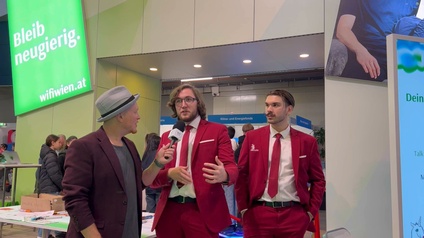 Zwei Personen in roten Anzügen werden von einer Person mit Hut und Mikrofon interviewt