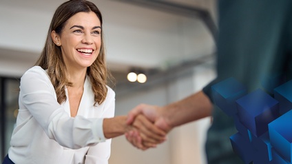 Zwei Personen reichen einander die Hände. Im Hintergrund ist ein Büroumfeld zu sehen. Das Gesicht einer Person ist sichtbar. Diese lächelt freudig. Rechts im Bild sind blaue Würfel darüber gelegt