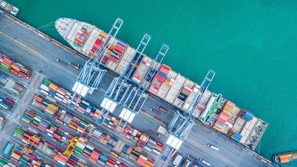 Luftaufnahme eines Containerfrachtschiffs, das zur Beladung in einem Hafen liegt.