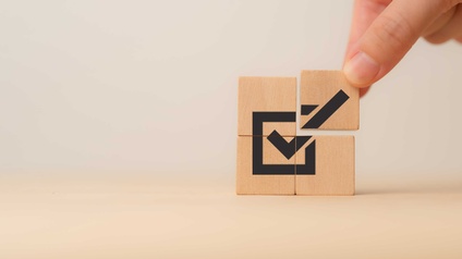 vier Holzklötzchen bilden aufeinandergesetzt eine angehakte Check-Box