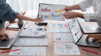 Blick auf einen Besprechungstisch mit Papierblättern auf denen farbige Diagramme und Grafiken abgebildet sind