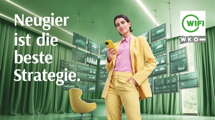 Eine Person in gelbem Anzug steht in einem grünen Raum mit Monitoren und hält ein Smartphone in der Hand. Darüber weißer Schriftzug Neugier ist die beste Strategie und dem WIFI-Logo.