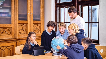 Lehrer erklärt Schülerinnen und Schüler etwas an einem Globus