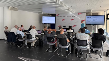 Ein Vortragssaal in dem mehrere Personen in Rückenansicht sitzen, vor ihnen hält einen stehende Person einen Vortag