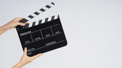 Hände halten eine Filmklappe vor einem hellen Hintergrund