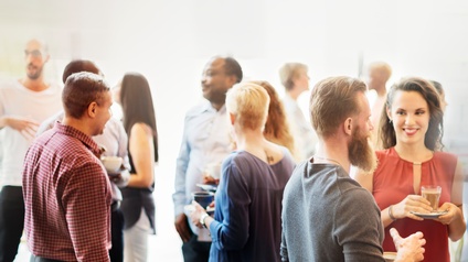 Gruppen von Personen stehen zusammen und unterhalten sich während einige von ihnen auch eine Kaffeetasse in Händen hält