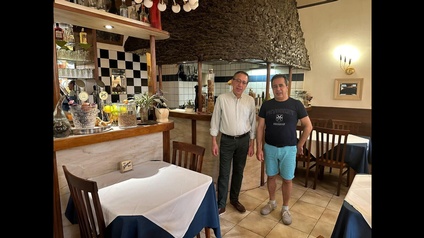 Zwei Personen stehen im Gästerbereich eines Restaurants, ringsum Tische mit Stühlen im Hintergrund und seitlich Theken