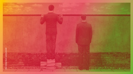 Zwei Personen stehen vor einer Wand, man sieht sie von hinten, die linke Person steht auf einem Stapel Bücher und schaut über die Mauer drüber