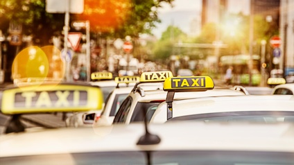 Hintereinander stehen ganz viele geparkte Autos. Auf jedem Auto ist oben ein Schild, in dem Taxi steht