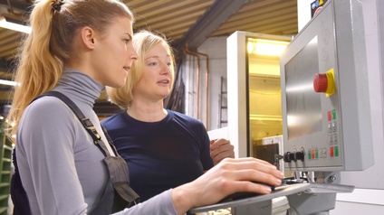 Zwei Personen stehen vor Monitor einer Anlagenregelung, eine Person hält Steuerungsmaus in Hand