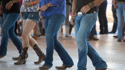 Detailansicht mehrerer Beinpaare in Jeans und Cowboystiefeln beim Linedancing